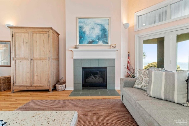 living room with a towering ceiling, a tile fireplace, and light hardwood / wood-style flooring