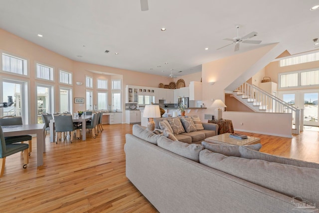 living room featuring french doors, a towering ceiling, ceiling fan, and light hardwood / wood-style flooring