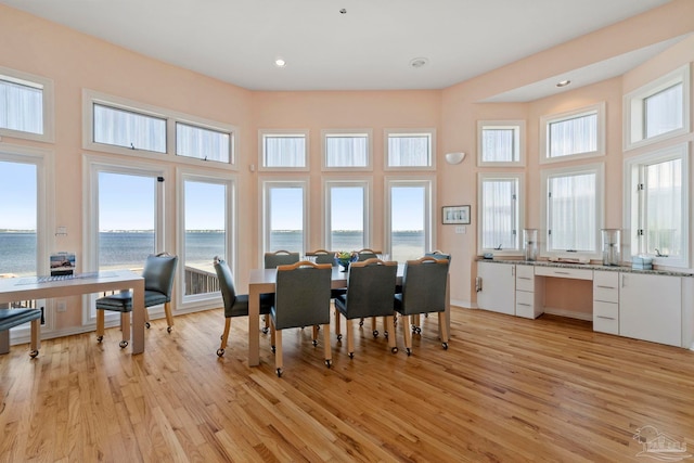 dining room featuring a water view, a towering ceiling, and light hardwood / wood-style floors