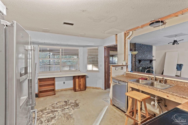 kitchen with a textured ceiling, concrete flooring, stainless steel appliances, a sink, and a brick fireplace