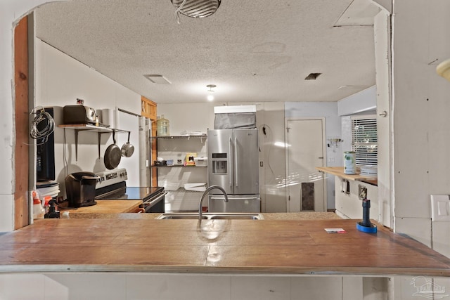 kitchen featuring a peninsula, stainless steel appliances, a textured ceiling, open shelves, and a sink