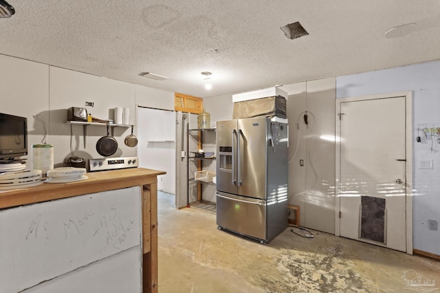 kitchen with concrete flooring, stainless steel fridge, wooden counters, and a textured ceiling