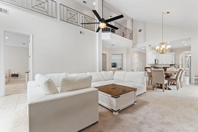 living room with visible vents, arched walkways, light colored carpet, high vaulted ceiling, and ceiling fan with notable chandelier