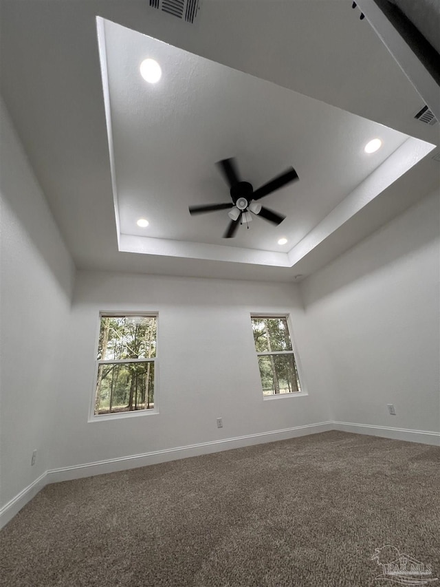 carpeted spare room with a raised ceiling, plenty of natural light, and ceiling fan