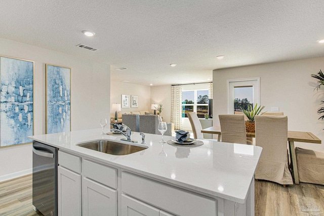 kitchen with an island with sink, white cabinets, a textured ceiling, light hardwood / wood-style flooring, and sink