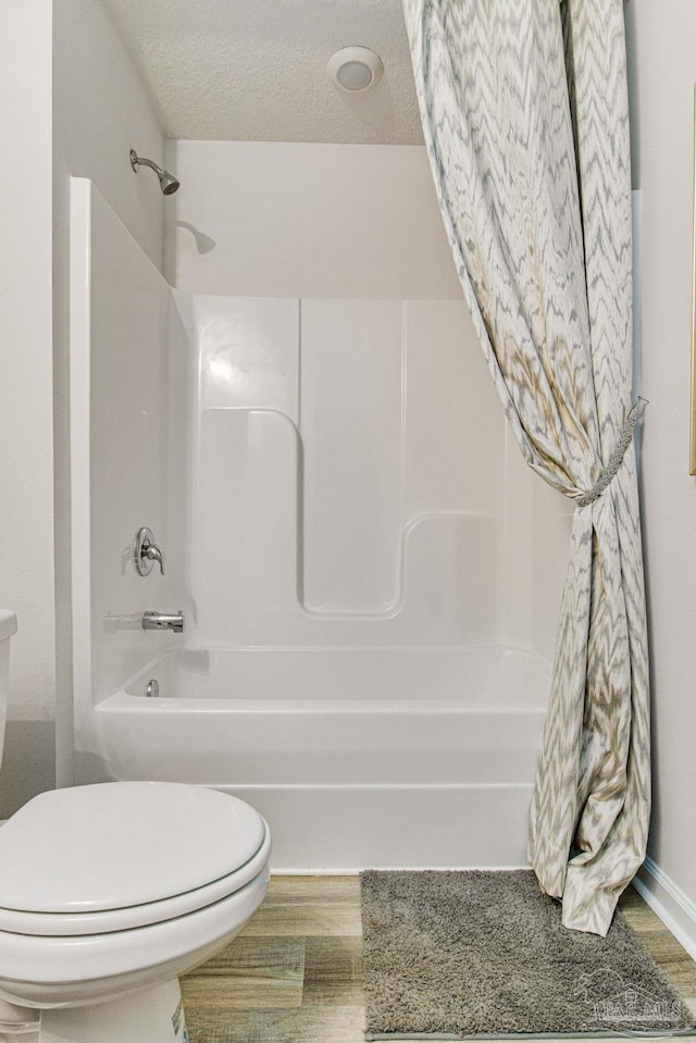 bathroom featuring wood-type flooring, a textured ceiling, toilet, and shower / bathtub combination with curtain