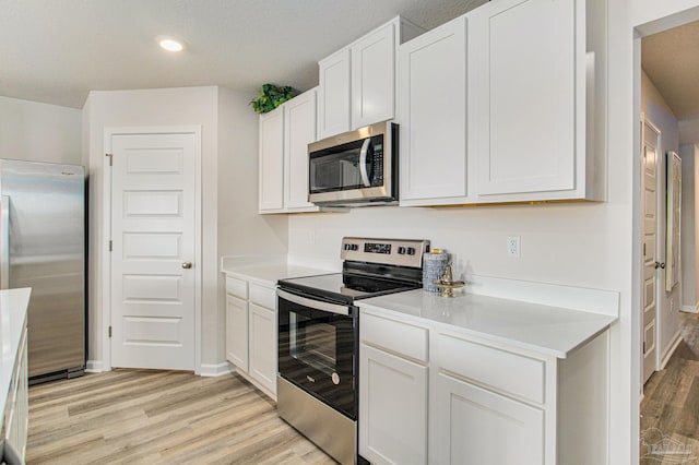 kitchen with light hardwood / wood-style flooring, a textured ceiling, stainless steel appliances, and white cabinetry