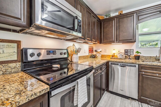 2543 Bayview Way, Pensacola, FL 32503 - kitchen featuring stainless steel appliances, dark brown cabinetry, light wood-type flooring, a sink, and light stone countertops