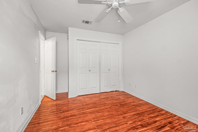 unfurnished bedroom with ceiling fan, a closet, a textured ceiling, and light hardwood / wood-style flooring