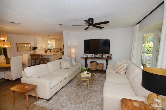 living room featuring ceiling fan, light hardwood / wood-style floors, and a textured ceiling