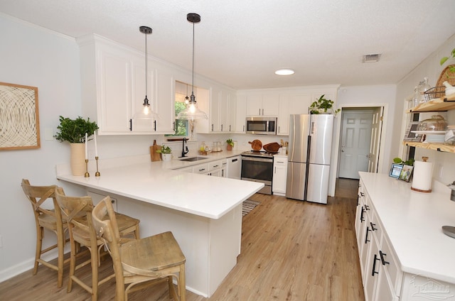 kitchen with hanging light fixtures, stainless steel appliances, kitchen peninsula, a breakfast bar, and white cabinets