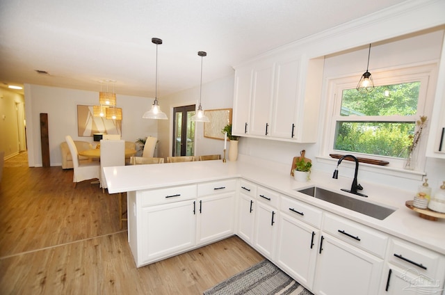 kitchen with kitchen peninsula, sink, white cabinets, and hanging light fixtures