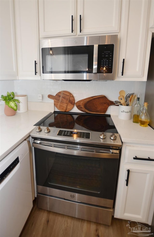 kitchen featuring dark hardwood / wood-style floors, decorative backsplash, white cabinetry, and appliances with stainless steel finishes