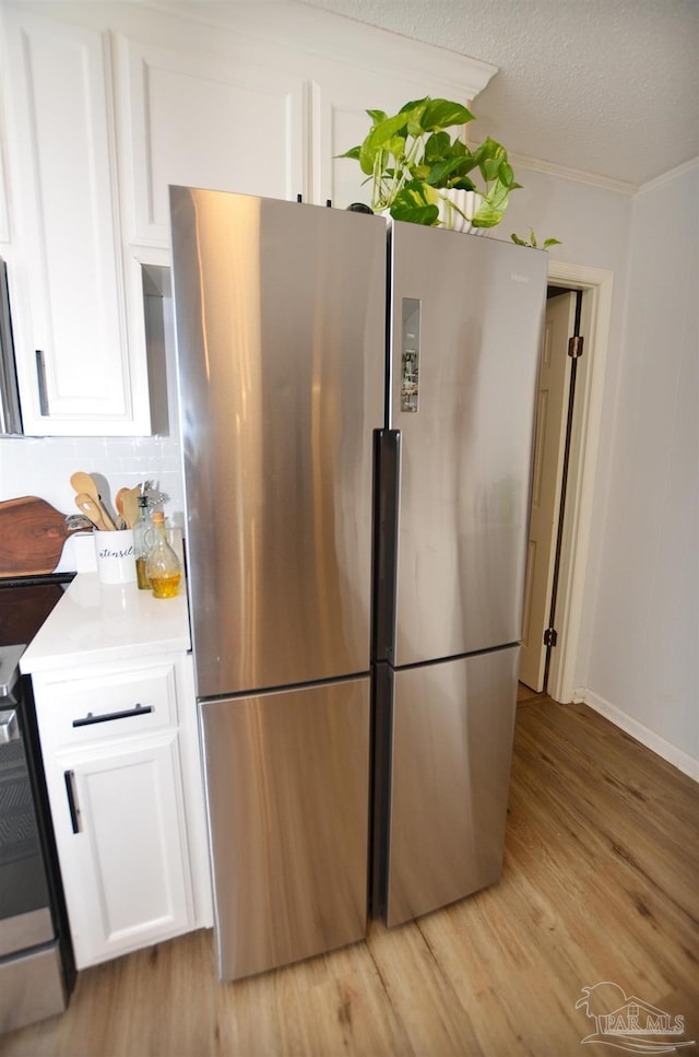 kitchen with white cabinets, decorative backsplash, light wood-type flooring, range, and stainless steel refrigerator