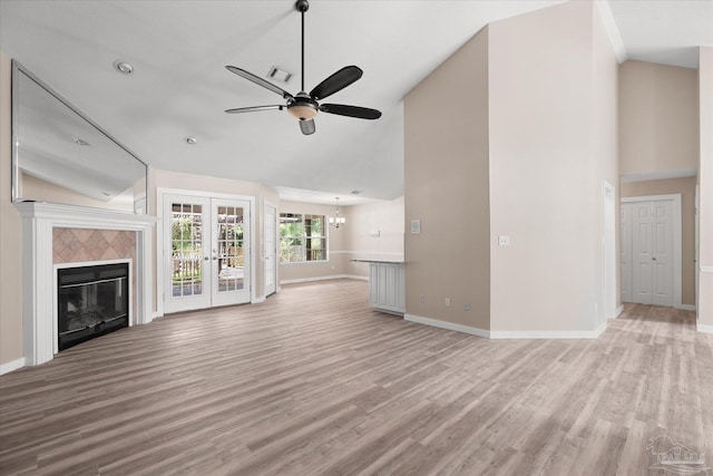 unfurnished living room featuring french doors, light hardwood / wood-style floors, lofted ceiling, a tiled fireplace, and ceiling fan with notable chandelier