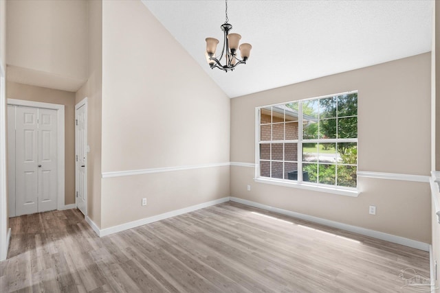 empty room featuring light wood-type flooring, a healthy amount of sunlight, vaulted ceiling, and a notable chandelier