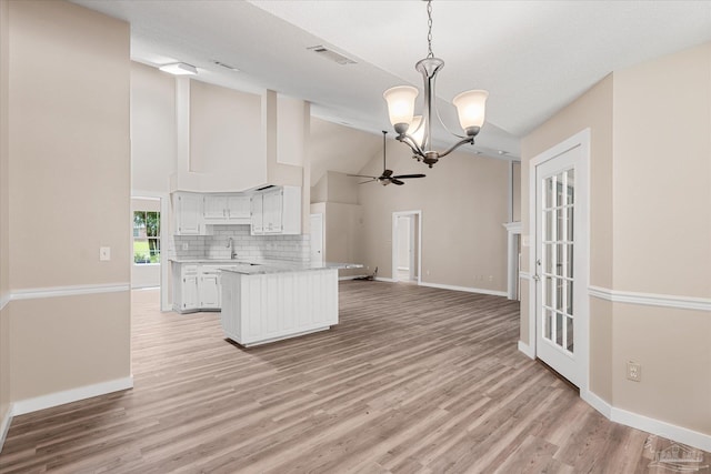 kitchen featuring kitchen peninsula, tasteful backsplash, pendant lighting, white cabinets, and lofted ceiling