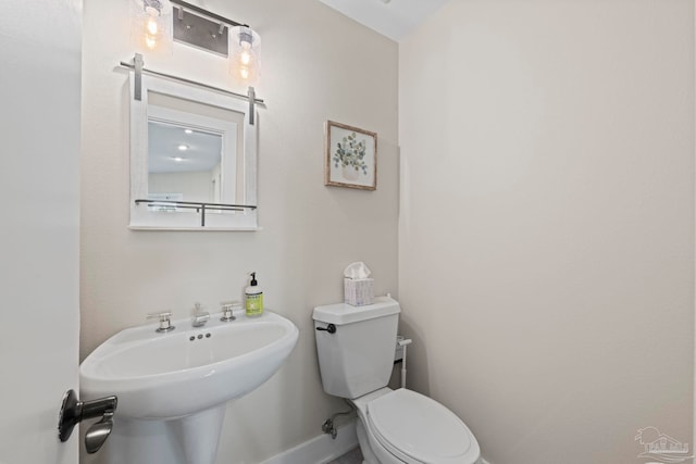 half bathroom with baseboards, a sink, and toilet