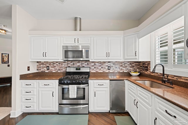 kitchen with dark wood finished floors, backsplash, appliances with stainless steel finishes, white cabinets, and a sink