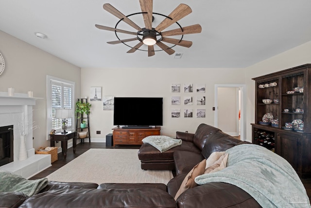 living area with ceiling fan, wood finished floors, visible vents, baseboards, and a tiled fireplace