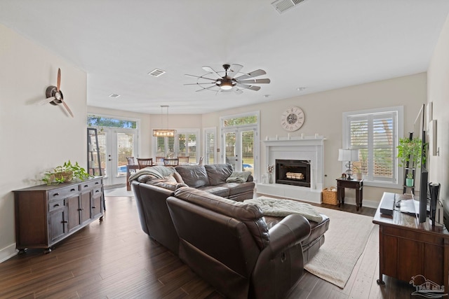 living room featuring a fireplace with raised hearth, dark wood-type flooring, visible vents, and a ceiling fan