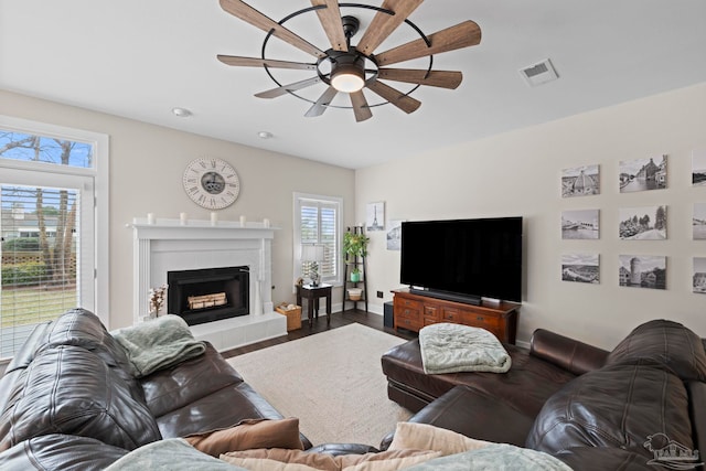 living area featuring ceiling fan, a tile fireplace, wood finished floors, visible vents, and baseboards