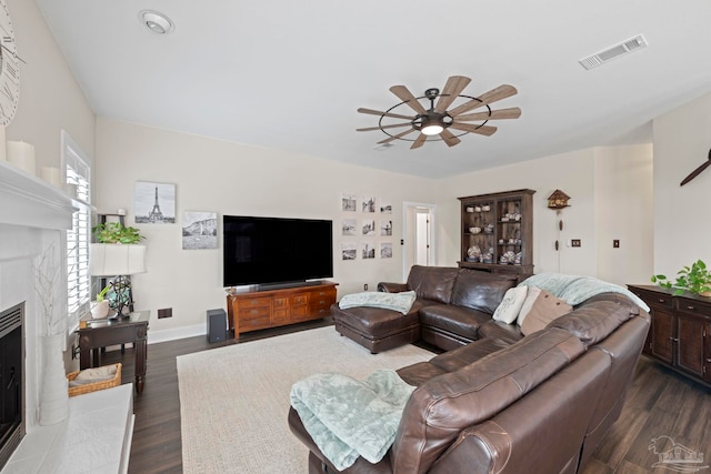 living room with ceiling fan, a fireplace, visible vents, baseboards, and dark wood-style floors