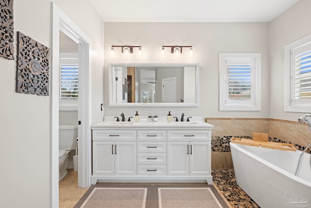 bathroom with double vanity, a soaking tub, a sink, and toilet