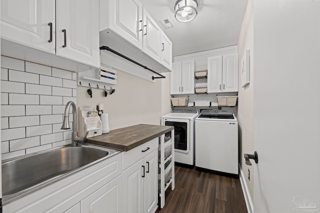 kitchen with washing machine and clothes dryer, decorative backsplash, white cabinetry, a sink, and wood counters