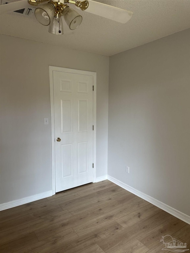 empty room featuring a ceiling fan, a textured ceiling, baseboards, and wood finished floors