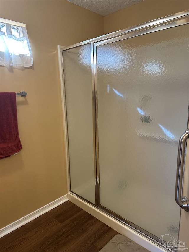 bathroom featuring baseboards, a shower stall, a textured ceiling, and wood finished floors