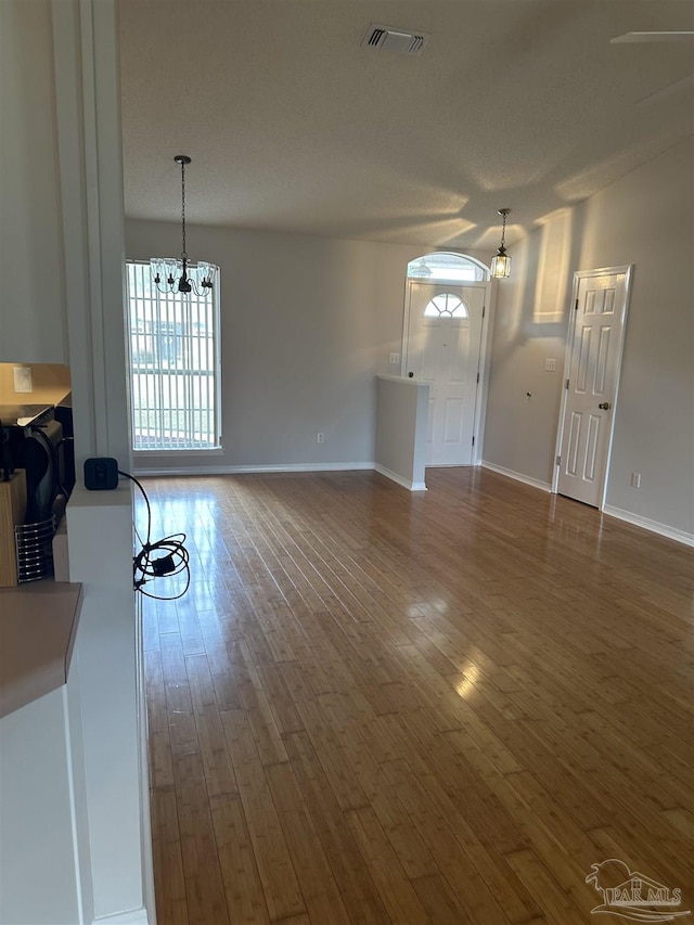 unfurnished living room with hardwood / wood-style flooring, baseboards, visible vents, and a notable chandelier