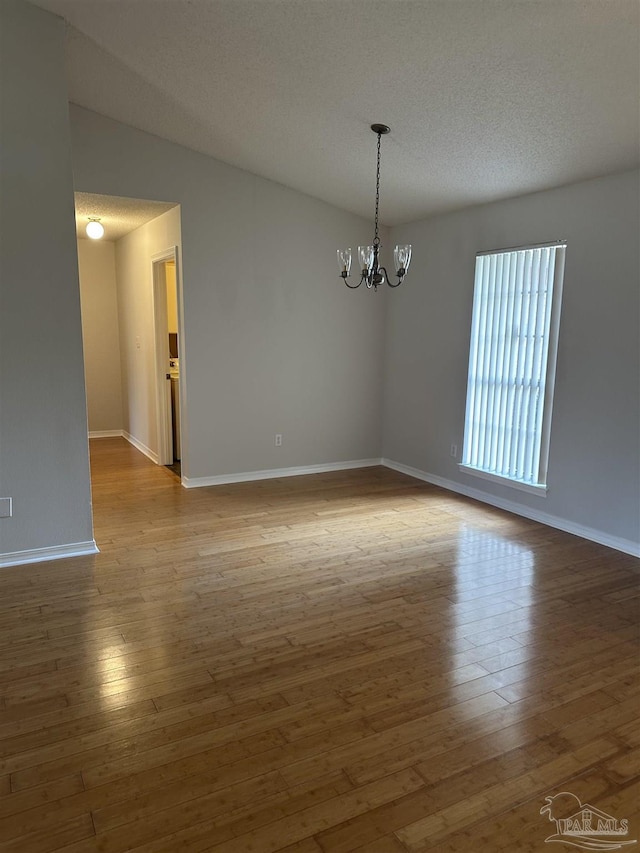 unfurnished room featuring an inviting chandelier, a textured ceiling, baseboards, and wood finished floors