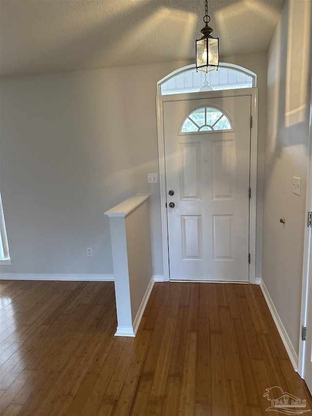 foyer featuring a textured ceiling, baseboards, and dark wood-type flooring