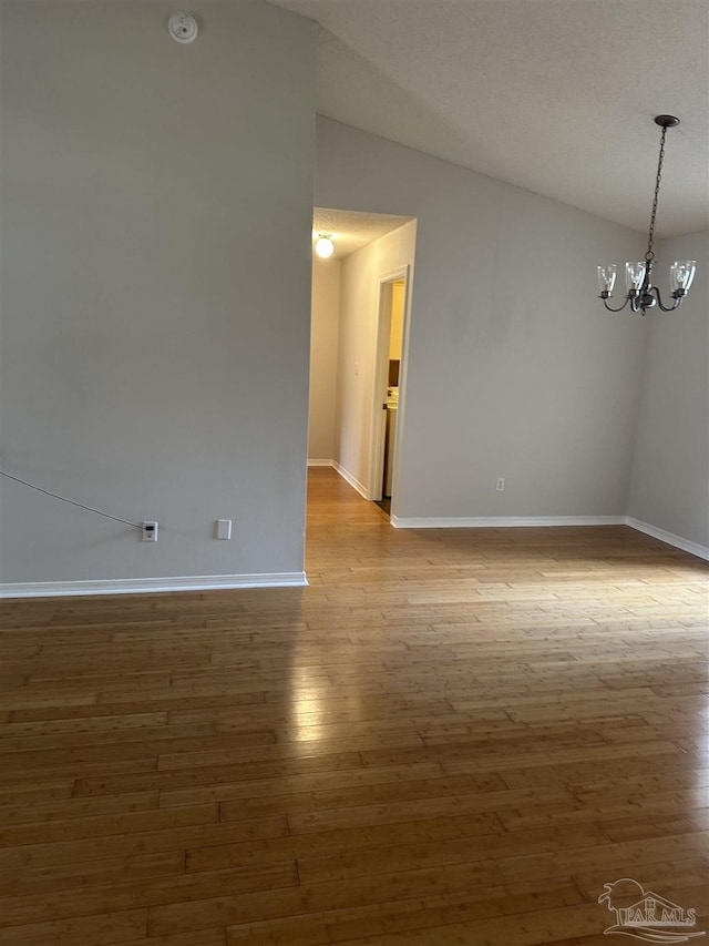 empty room with a notable chandelier, baseboards, vaulted ceiling, and wood finished floors