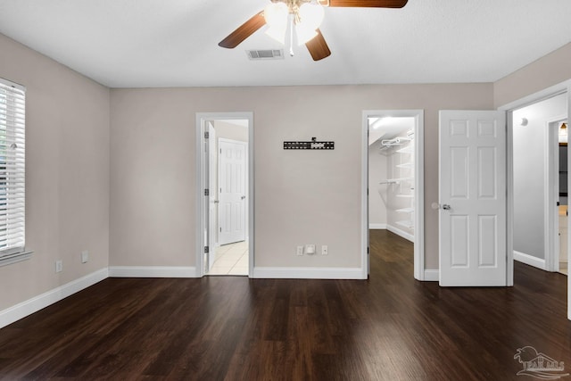 unfurnished bedroom featuring a spacious closet, dark hardwood / wood-style floors, and ceiling fan