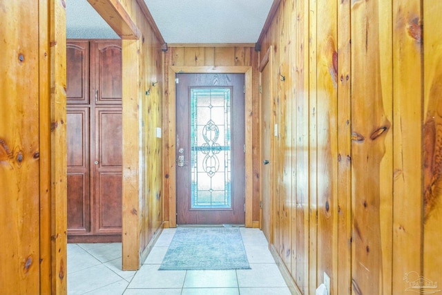 doorway featuring wood walls, light tile patterned floors, and a textured ceiling