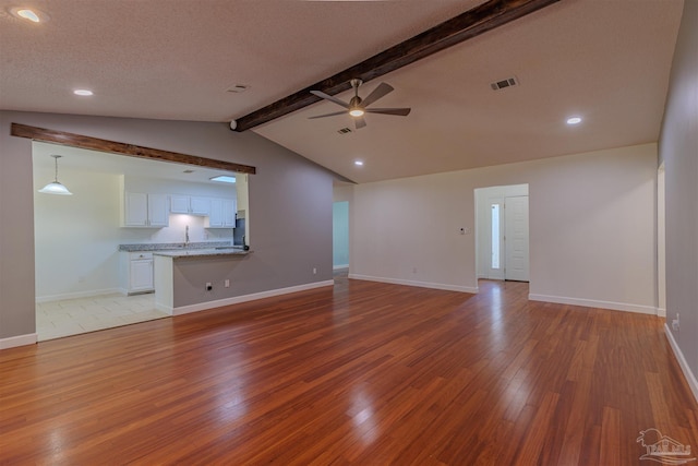 unfurnished living room featuring ceiling fan, light hardwood / wood-style flooring, lofted ceiling with beams, and a textured ceiling