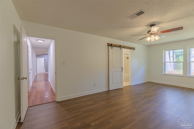 empty room featuring ceiling fan, a barn door, dark hardwood / wood-style floors, and a textured ceiling