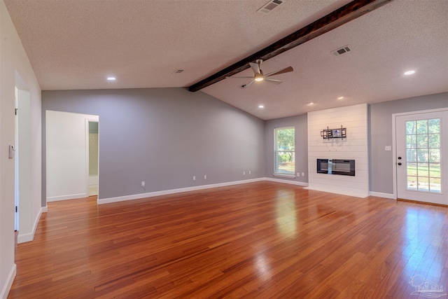 unfurnished living room with a large fireplace, light hardwood / wood-style floors, lofted ceiling with beams, and a textured ceiling