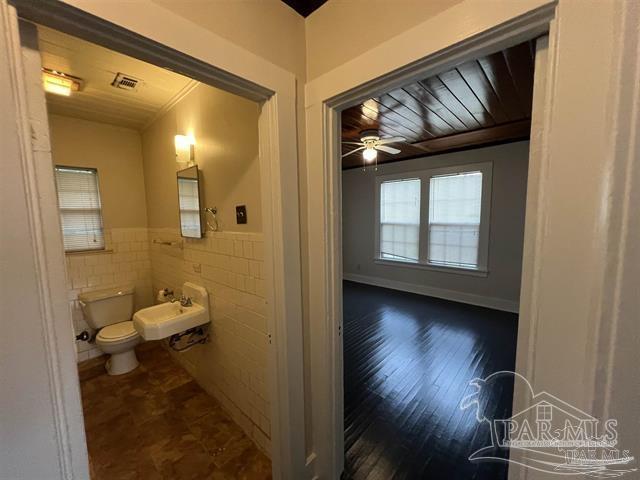 bathroom with a wainscoted wall, tile walls, visible vents, toilet, and a sink