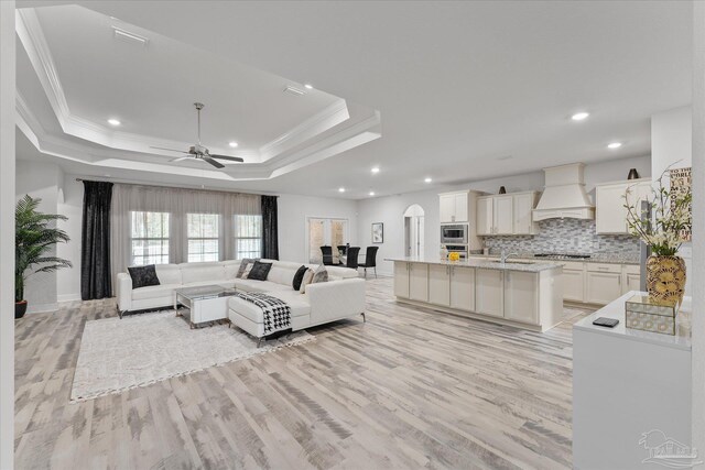 living room featuring crown molding, ceiling fan, a raised ceiling, and light wood-type flooring