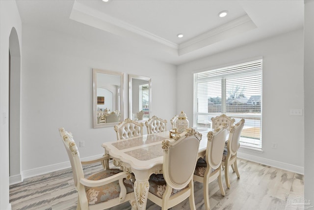 dining room featuring ornamental molding, a raised ceiling, and light wood-type flooring