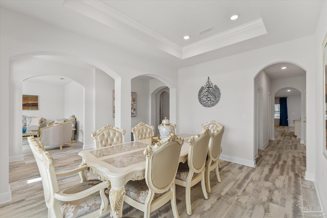 dining area with ornamental molding, a tray ceiling, and light wood-type flooring