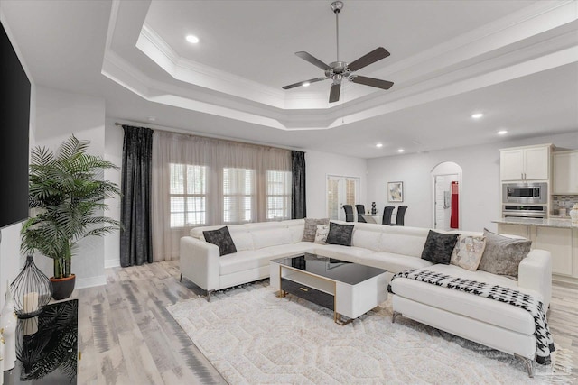 living room featuring crown molding, light hardwood / wood-style floors, a raised ceiling, and ceiling fan