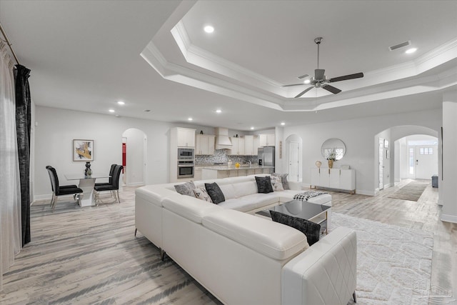 living room featuring crown molding, ceiling fan, light wood-type flooring, and a tray ceiling