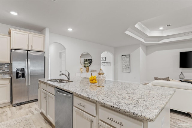 kitchen featuring a kitchen island with sink, sink, stainless steel appliances, and light stone countertops