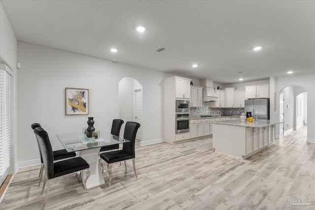 kitchen featuring appliances with stainless steel finishes, a center island, light stone countertops, decorative backsplash, and custom exhaust hood