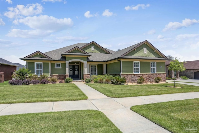 craftsman house featuring a shingled roof, stone siding, and a front yard