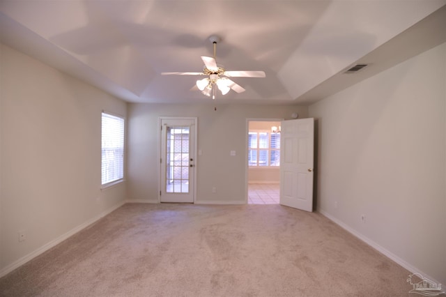 spare room with a raised ceiling, ceiling fan, and light colored carpet